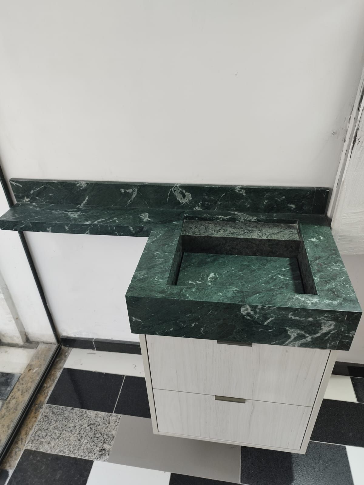 Bancada com cuba esculpida em mármore verde sobre marcenaria clara.